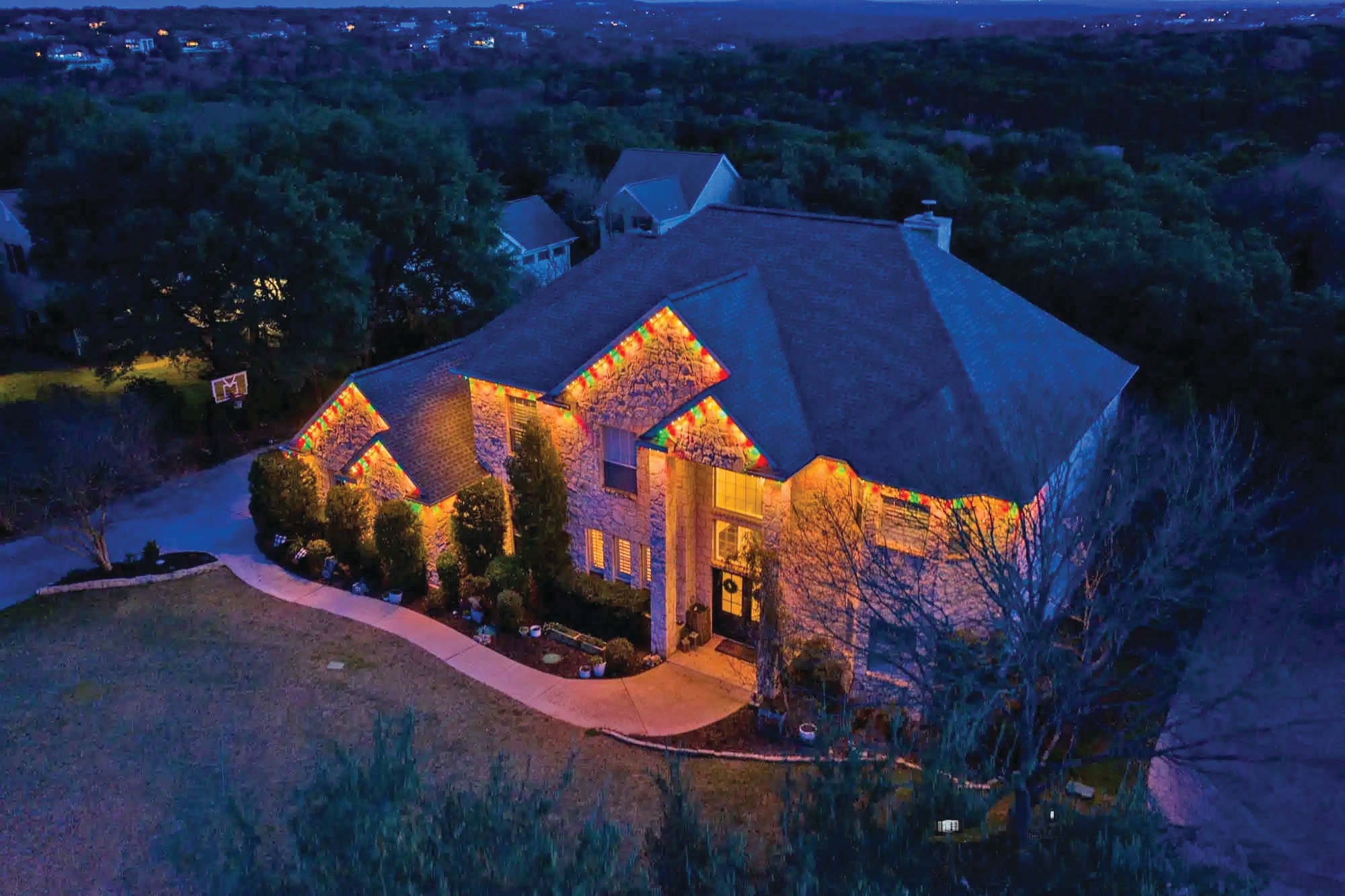 Aerial view of stone home with multicolor Gemstone Lights